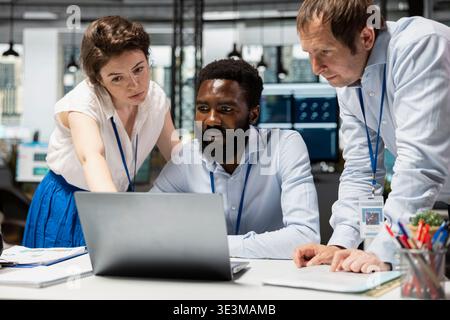 Beschäftigte Mitarbeiter arbeiten zusammen, um Dokumente auf dem Laptop auszuwerten. Schwarzer Mann mit kaukasischen Kollegen, die ihre beruflichen Fähigkeiten teilen, um die Unternehmensinvestitionen zu verbessern. Teamarbeit im Büro. Stockfoto