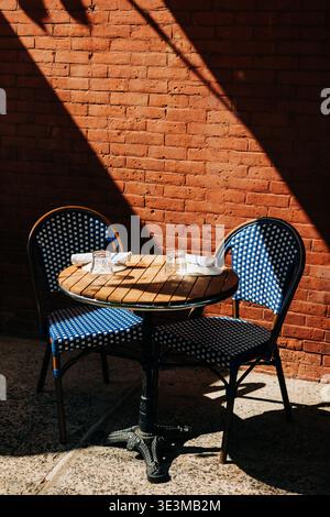 Leerer Tisch mit blauen Stühlen im Freien mit gemauerter Wand und Schatten bei hellem Tageslicht Stockfoto