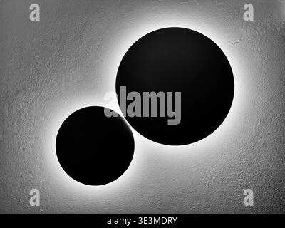 Architektonische Abstraktion von zwei Leuchten an einer Wand ähnelt dem Mond, der die Erde umkreist. Stockfoto