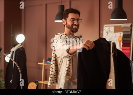 Männlicher Schneider, der nachts Kleidung vom Regal im Atelier nimmt Stockfoto