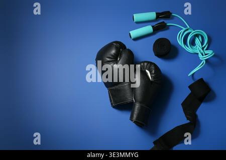 Ein Paar schwarze Boxhandschuhe mit Armbändern und Sprungseil auf blauem Hintergrund Stockfoto