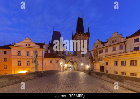Altstädter Brückenturm an der Karlsbrücke in Prag, Tschechische Republik, bei Sonnenaufgang mit beleuchteten Fassaden und leerer Kopfsteinpflasterstraße. Stockfoto
