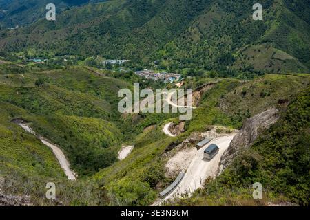 Lkw fahren kurvenreiche, unbefestigte Straßen durch zerklüftete grüne Berge, die zu einem kleinen Dorf im Tal führen, das abgelegene Reisen und ländliche Gebiete hervorhebt Stockfoto