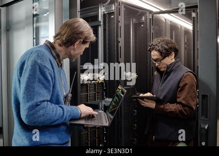 Kaukasier mittleren Alters und junger erwachsener Mann, der Server-Geräte verwaltet Stockfoto