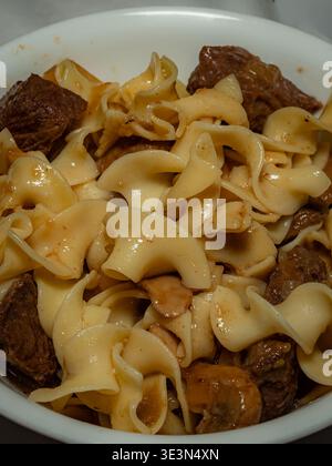 Ein Makroblick von oben nach unten auf eine Schüssel mit Rindfleisch-Stroganoff mit breiten Eiernudeln und Steak-Stücken in einer cremigen Pilzsauce Stockfoto