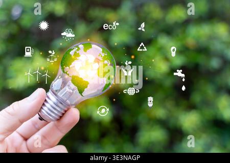 Nahaufnahme einer Hand, die eine Glühbirne mit Ikonen Erde, Recycling und grüne Energie auf Naturhintergrund hält, die Nachhaltigkeit, erneuerbare Energie symbolisieren, Stockfoto
