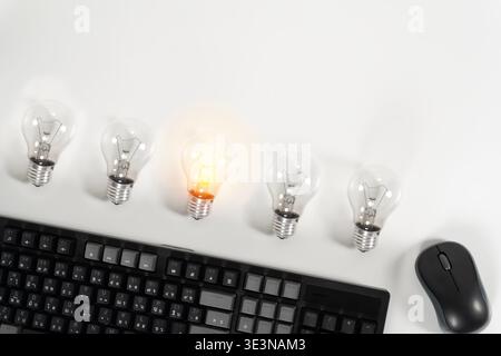 Draufsicht auf Tastatur, Maus und fünf Glühbirnen, von denen eine auf weißem Hintergrund leuchtet, symbolisiert kreative Idee, Innovation, Problemlösung, Büro Stockfoto