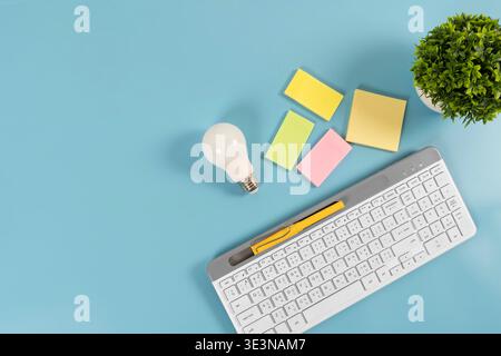 Draufsicht auf Tastatur, LED-Lampe, Haftnotizen, Stift und Pflanze auf blauem Hintergrund mit Kopierraum, symbolisiert Büroplanung, Ideen, Produktivität, Orga Stockfoto