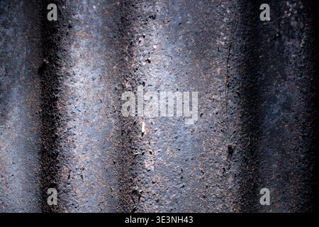 Makroaufnahme aus altem, schmutzigem und stark rostigem dunklem Wellblech mit vertikalen Wellen und verwitterter Textur unter kontrastreicher Seitenbeleuchtung. Stockfoto