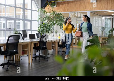 Verschiedene weibliche Kollegen, die mit einer Einkaufstasche im Büro unterwegs sind und Kaffee trinken, Telefon und Kopierraum überprüfen Stockfoto