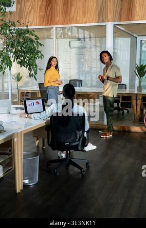 Verschiedene Kollegen in Bürokleidung diskutieren Ideen am Arbeitsplatz mithilfe von Laptopkarten und Whiteboard Stockfoto