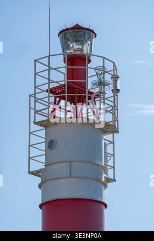 Ein rot-weißer Leuchtturm aus Metall mit einem Glaslaternenraum, Sicherheitsgeländern und Navigationslichtern, die vor einem klaren blauen Himmel stehen und an coa erinnern Stockfoto