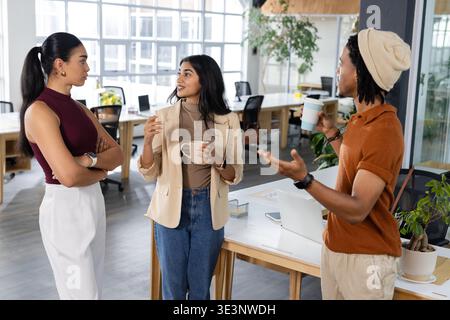 Verschiedene Kollegen diskutieren über das Projekt, während sie im Großraumbüro Kaffeetasse und Tassen zum Mitnehmen halten Stockfoto