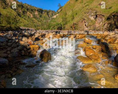 Rauschendes Wasser, das über bunte Felsen in einem steilen Bergtal unter blauem Himmel stürzt Stockfoto