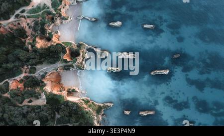 Aus der Vogelperspektive treffen auf das türkisfarbene Meer mit verstreuten Felsformationen, die von oben sichtbar sind, Alvor, Faro District, Portugal. Stockfoto