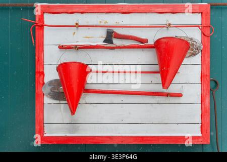 An der Wand hängen zwei konische Feuereimer und eine Feueraxt mit rotem Griff. Stockfoto