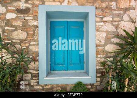 Traditionelles blaues Fenster auf Steinmauer in Pythagoreio – mediterrane Architektur, griechischer Inselreisehintergrund Stockfoto