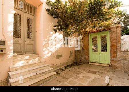 Sonnendurchfluteter traditioneller Innenhof mit pastellfarbenen Türen in Vathy – authentische griechische Architektur, mediterrane Lifestyle-Szene Stockfoto