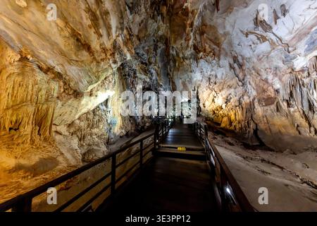 Blick auf einen Holzsteg, der durch das Herz eines höhlenartigen Raumes führt, beleuchtet von warmem Licht, das von den strukturierten Kalksteinformationen reflektiert wird, P Stockfoto