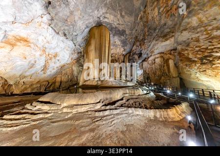 Blick auf geschichtete Felsformationen und einen hölzernen Fußweg, beleuchtet von Lichtern, die durch die Dunkelheit in der Paradies Cave, Phong Nha, Quang Binh, Vietn schneiden Stockfoto