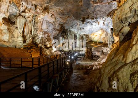 Blick auf eine riesige Höhle, beleuchtet von Scheinwerfern, enthüllt komplexe Felsformationen und einen hölzernen Fußweg, der durch die Paradise Cave, Phong Nha führt Stockfoto