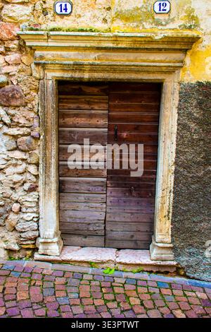 Alte braune Holztür mit Pfosten und Portal aus farbigem Porphyr geschnitztem Marmor und gelber Wand zwei Hausnummern über dem Portal Stockfoto
