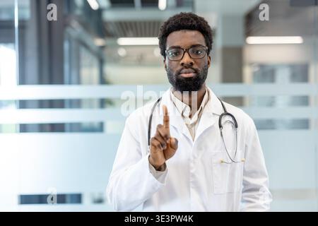 Vertrauenswürdiges medizinisches Fachpersonal, das einen Labormantel und ein Stethoskop trägt und mit dem Zeigefinger eine „Nein“- oder „Vorsicht“-Geste macht, was Fachwissen und repräsentiert Stockfoto
