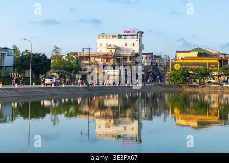 Hue City, Vietnam - 24. Januar 2026: Blick auf das ruhige Wasser, das die lebhaften Gebäude und die belebte Straße von Hue City widerspiegelt, eine friedliche Szenerie Stockfoto