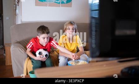 Kinder schauen sich Fußballspiele im fernsehen an und essen Popcorn Stockfoto