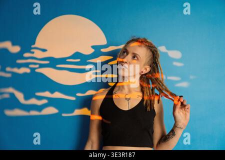 Frau mit Dreadlocks und Tattoos, die sich unter projiziertem Licht und Mondwandkunst posiert Stockfoto