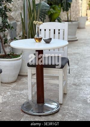 Terrasse mit weißem Tisch und Stuhl, dekorativer Vase mit Blumen und Topfpflanzen. Mobiles Foto Stockfoto