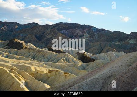 Erodierte Wüstenhügel und mehrschichtige Bergkämme unter teilweise bewölktem Himmel in trockenem Badland bei Tageslicht Stockfoto