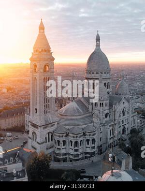 Blick aus der Vogelperspektive auf die Basilika Sacré-Cœur, die im warmen Glanz des Sonnenaufgangs getaucht ist, deren weißer Stein sich von den sanften Farbtönen des Pariser Sonnenaufgangs, Par, abhebt Stockfoto