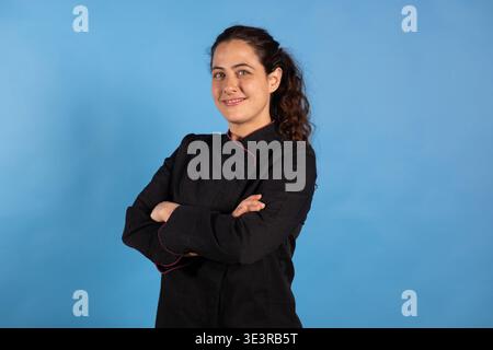 Selbstbewusste Chefkochin in schwarzer Uniform mit überkreuzten Armen Stockfoto