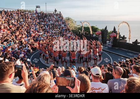 Eine Gruppe von Künstlern zeigt einen traditionellen Kecak-Tanz im Uluwatu-Tempel auf Bali. Viele Menschen beobachten und fotografieren, während die Sonne untergeht Stockfoto