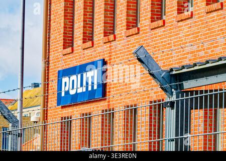Stacheldrahtzaun und Sicherheitstor aus Metall schützen an einem sonnigen Tag das dänische Politi-Polizeischild mit blauem Schild unter klarem Himmel. Stockfoto