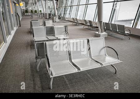 Eine leere Abfluglounge in einem modernen Flughafenterminal verfügt über Sitzreihen aus perforiertem Metall. Stockfoto