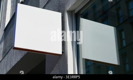 Mockup-Vorlage für Werbeflächen für Werbekampagnen und Marketingkampagnen Ein weißes quadratisches Schild hängt am Gebäude neben einem Fenster wi Stockfoto