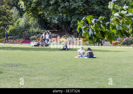 Menschen, die sich auf grünem Gras in einem öffentlichen Park entspannen. London, UK, 23. Juli 2023 Stockfoto