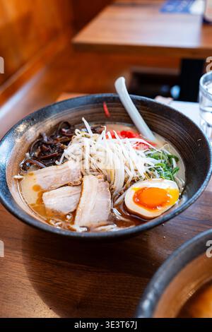 Eine Schüssel Tonkotsu-Ramen mit geschnittenem Chashu-Schweinefleisch, mariniertem Ei, frischen Sprossen und eingelegtem Ingwer auf einem rustikalen Holz Stockfoto