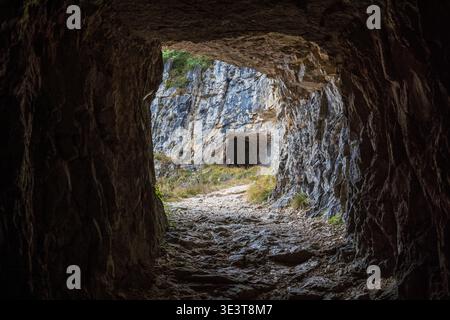 Eindrucksvoller Schuss aus einem in Felsen gehauenen Tunnel an der 52 Tunnels Road, Mount Pasubio. Der Schotterweg führt zu einer weiteren Öffnung im Berg massi Stockfoto