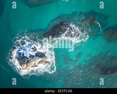 Aus der Vogelperspektive auf das türkisfarbene Meer und die felsige Küste in Sommaroy, Norwegen, Wellen, die im klaren arktischen Wasser auf Felsen stürzen. Stockfoto