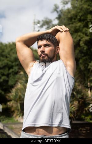 Junger athletischer Mann, der sich vor dem Training in einem Park ausdehnt. Gesunder Lebensstil, Outdoor-Fitnesstraining und Aufwärmroutine in einer natürlichen Umgebung. Stockfoto