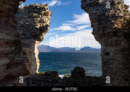 Blick auf den Gardasee durch antike Steinruinen, natürliche Felswände mit Bergen und blauem Himmel, malerische italienische Reisesandschaft. Stockfoto