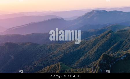 Blick aus der Vogelperspektive auf die mehrschichtigen Bergketten bei Sonnenuntergang oder Sonnenaufgang mit farbenfrohem Himmel und nebeliger Landschaft Stockfoto