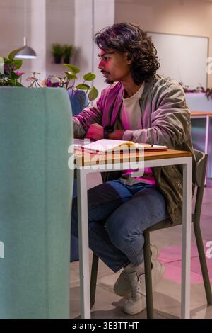 Indischer Mann, der an einem Laptop arbeitet, im Co-Working-Raum auf einem Holztisch mit Notebook, Stift, Armbanduhr Stockfoto