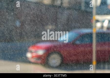 Abstrakte Straßenszene, die durch schmutziges Fenster mit Staub und Schmutz betrachtet wird, zeigt ein verschwommenes rotes Auto und urbanes Hintergrund in weichem Fokus Stockfoto