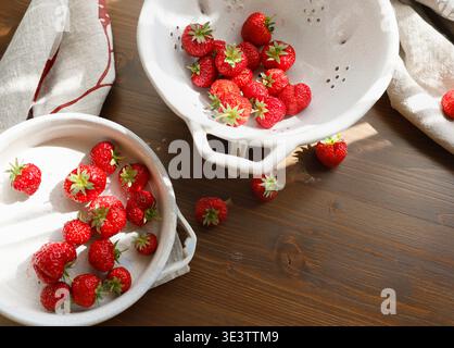 Frische rote Erdbeeren in weißer Keramik Vintage Schüssel auf dunklem Holztisch. Ästhetische Lebensmittelfotografie zeigt Bio-Sommerbeeren für ein langsames Leben Stockfoto