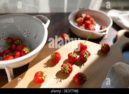 Frische rote Erdbeeren auf hölzernem Schneidebrett in hellem Morgensonnenlicht. Die ästhetische Lebensmittelfotografie erfasst Bio-Sommerbeeren und rustikale Stockfoto