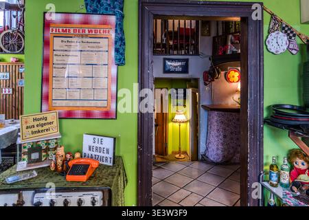 Der Eingangsbereich des Restaurants Kollektiv Leipzig ist im DDR-Stil eingerichtet: Grüne Wände, ein „Film der Woche“-Hinweis, russische Matryoschka-Puppen, ein orange-rotes Drehwahltelefon und ein Schild mit der Aufschrift „Bitte nehmen Sie Platz“. Leipzig, Sachsen, Deutschland Stockfoto